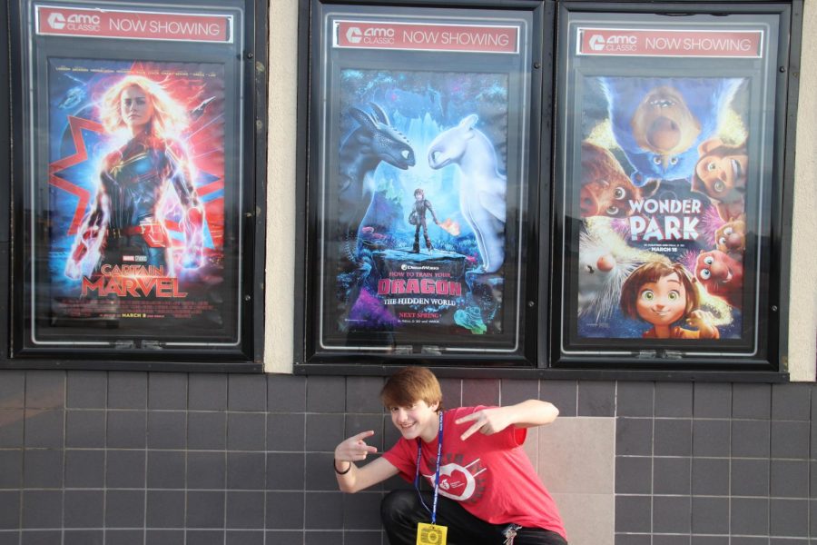 Reviewer Mac Hardy poses in front the How to Train your Dragon: Hidden World movie poster.